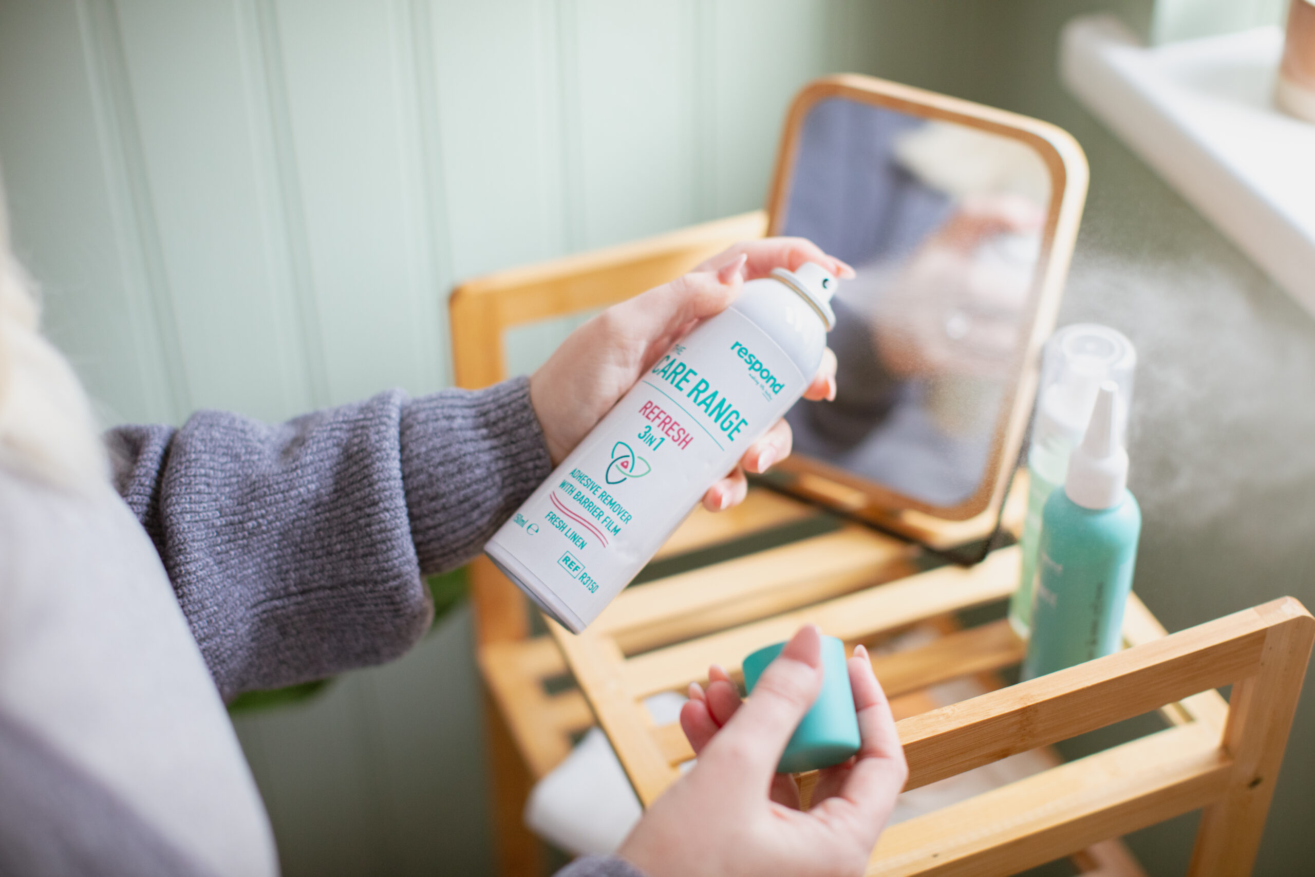 2M2A7445 A user sprays REFRESH 3in1 spray in their bathroom, with other Respond products on display in the background.