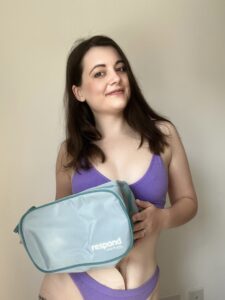 Amy poses in purple underwear, smiling, while holding her Respond stoma bag.